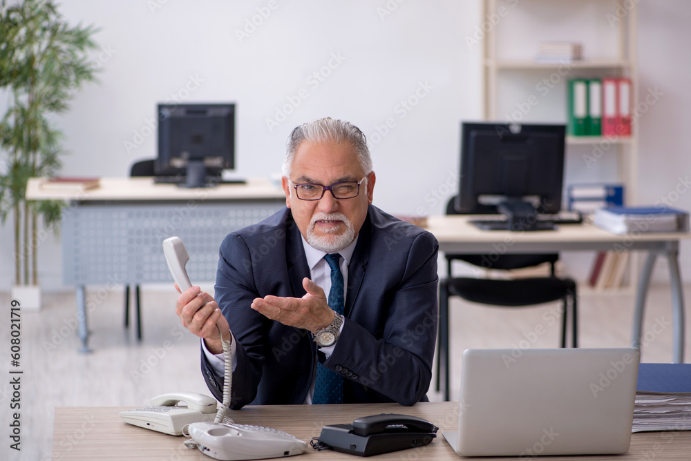 Old male employee speaking on the phone at workplace