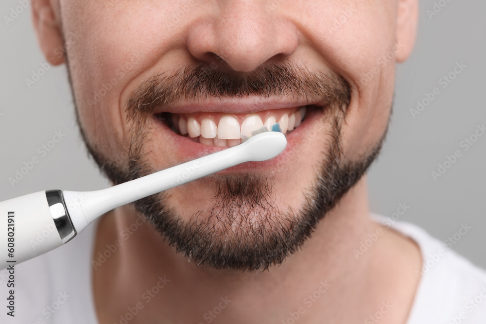 Naklejka premium Man brushing his teeth with electric toothbrush on light grey background, closeup