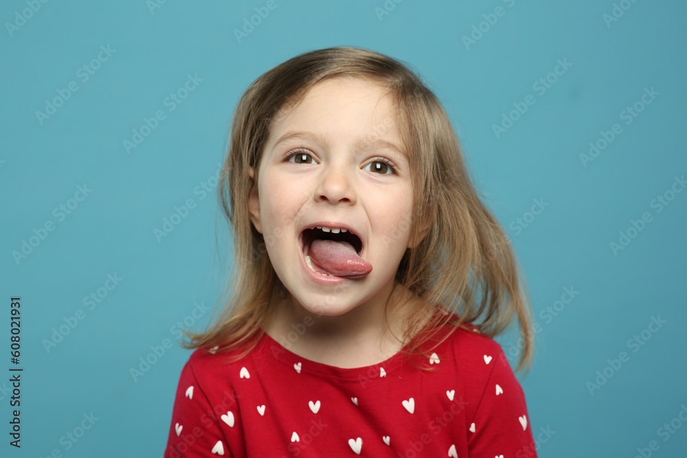 Funny little girl showing her tongue on light blue background - obrazy, fototapety, plakaty 