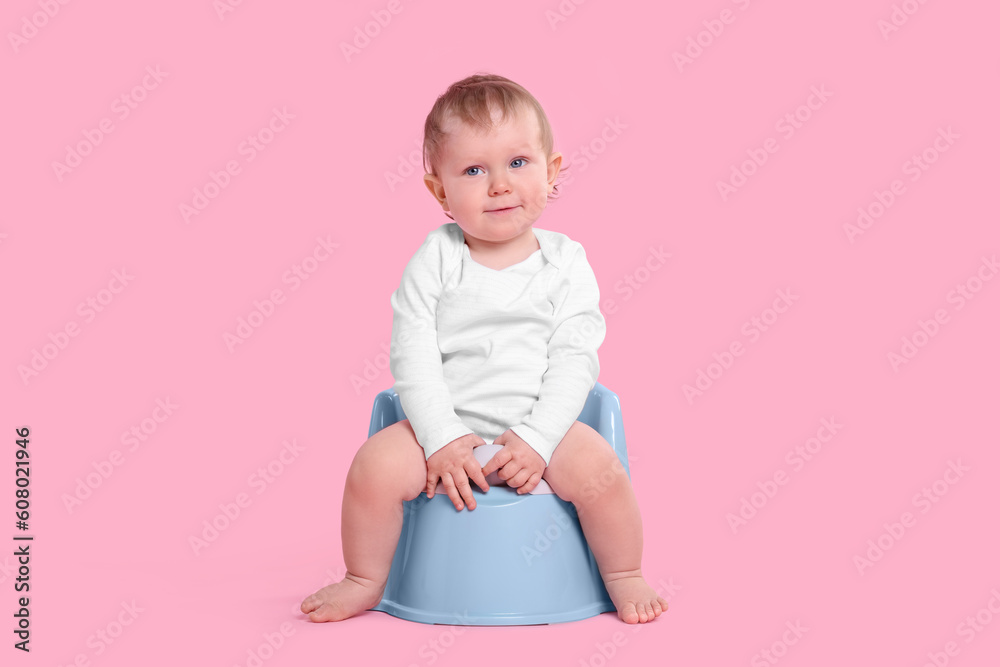 Little child sitting on baby potty against pink background Little child sitting on baby potty against pink background