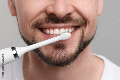Man brushing his teeth with electric toothbrush on light grey background, closeup