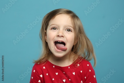 Tableau sur toile Funny little girl showing her tongue on light blue background