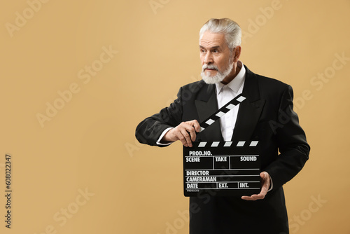 Senior actor holding clapperboard on beige background, space for text. Film industry