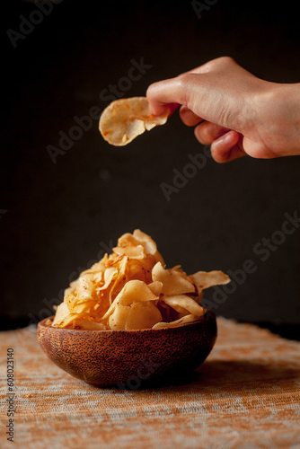 Keripik singkong. Cassava chips or tapioca chips is traditional snack from Java, made of cassava thinly sliced and fried. Served in wooden bowl and black background for dark concept photo