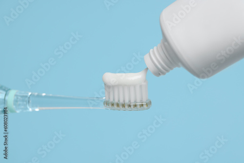 Squeezing toothpaste onto electric toothbrush on light blue background, closeup