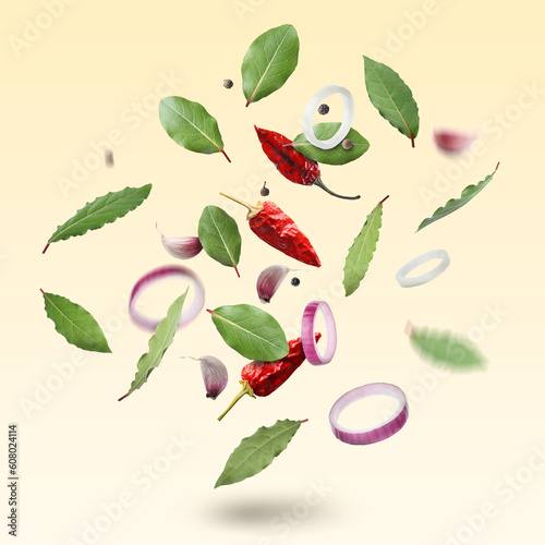 Bay leaves, onion rings, garlic cloves, dry red and black peppers falling on pale yellow gradient background