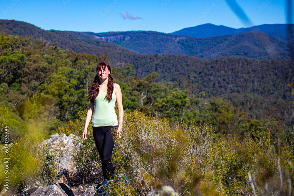 A beautiful girl celebrates a successful climb of the Pages Pinnacle and enjoys the view while standing on the narrow Razorback ridge. Hidden gems in Springbrook National Park, Gold Coast, Queensland 