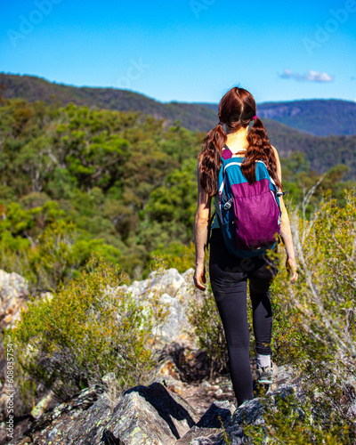 A beautiful girl celebrates a successful climb of the Pages Pinnacle and enjoys the view while standing on the narrow Razorback ridge. Hidden gems in Springbrook National Park, Gold Coast, Queensland 