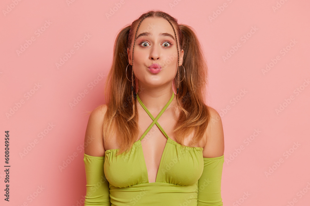 Funny girl poses on pink background, wearing green top and ponytails hairstyle, sending air kiss to camera, happy life concept, copy space Funny girl poses on pink background, wearing green top and ponytails hairstyle, sending air kiss to camera, happy life concept, copy space
