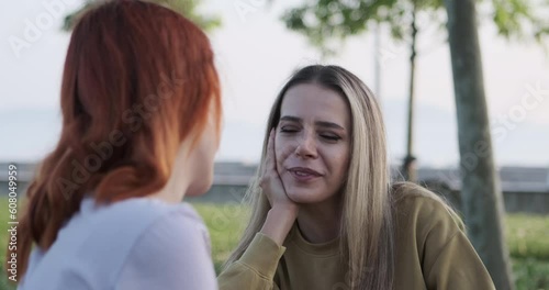A young woman sitting in the park, engaging in a delightful conversation with her girlfriend.