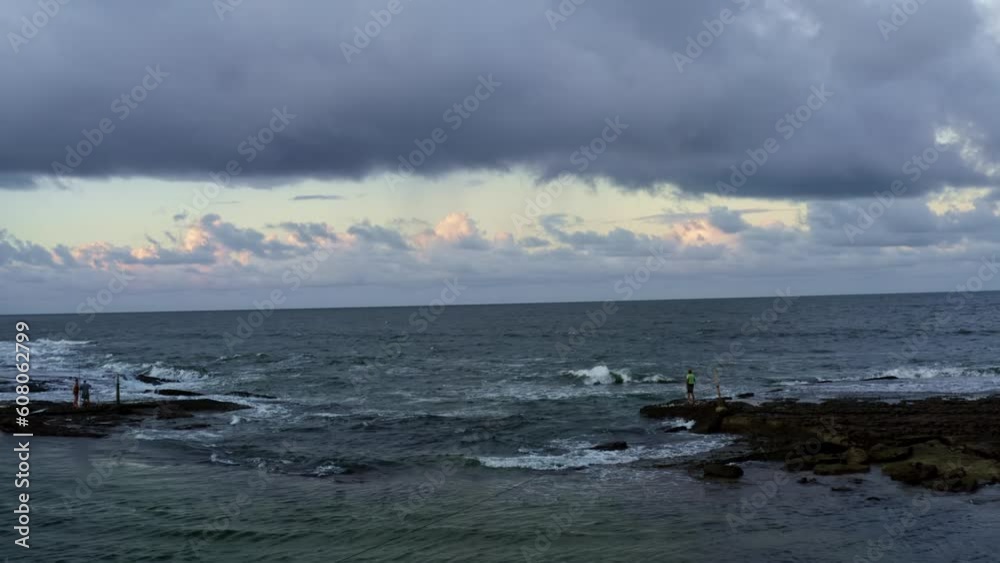 Dolly in aerial drone shot of people standing on exposed rocks that are blocking the waves and creating natural pools on Sibauma beach in Tibau do Sul, Rio Grande do Norte, Brazil on a summer evening. Dolly in aerial drone shot of people standing on exposed rocks that are blocking the waves and creating natural pools on Sibauma beach in Tibau do Sul, Rio Grande do Norte, Brazil on a summer evening.