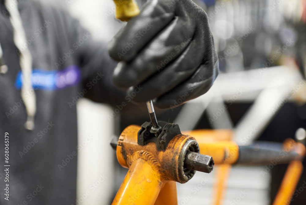 Maintenance of a bicycle: unknown man using protective gloves disassembling an orange bike at his repair shop. Maintenance of a bicycle: unknown man using protective gloves disassembling an orange bike at his repair shop.