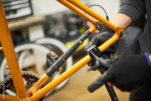 Repair of a bicycle: hands of an unrecognizable person using gloves disassembling an orange bike in his workshop. Selective focus composition.