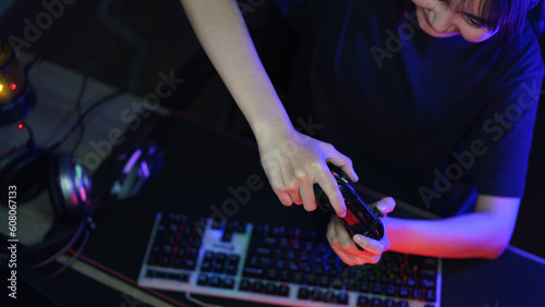 Female cyber hacker gamer playing or streaming video games on computer with joystick in neon light