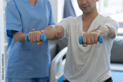 Physiotherapist giving therapy exercise with dumbbell equipment on male patient athlete arm and shoulder, physiotherapy concept, health insurance.