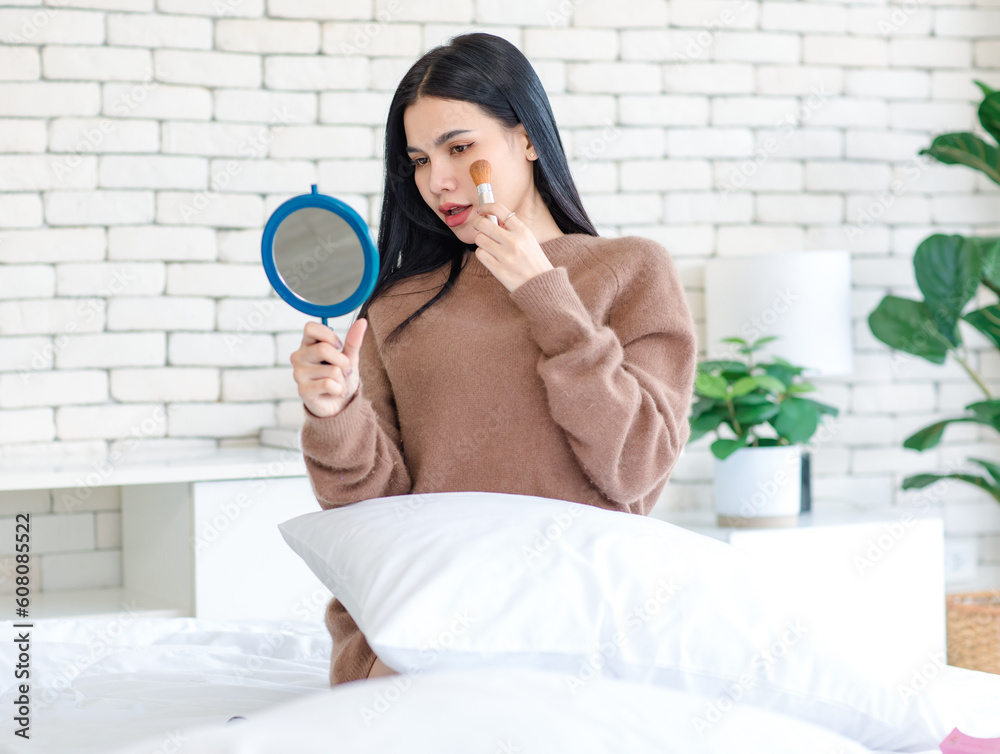 Millennial Asian beautiful cheerful happy female model in casual long sleeve sweater shirt outfit sitting smiling using brush on brushing cosmetic on cheek looking reflection from handheld mirror Millennial Asian beautiful cheerful happy female model in casual long sleeve sweater shirt outfit sitting smiling using brush on brushing cosmetic on cheek looking reflection from handheld mirror