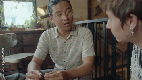 Young Asian antique store owner telling history of old pendant to female customer. Over-the-shoulder shot photo