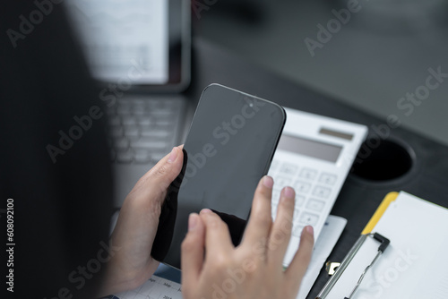 Young business woman on the phone at the office.Business woman texting on the phone and working on laptop.Beautiful young business woman sitting in office.Business woman smiling.
