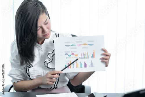 Young successful employee business woman white shirt hold paper account documents work stand at workplace white desk with laptop pc computer at light modern office indoors achievement career concept
