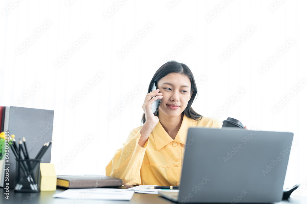 Young business woman on the phone at the office.Business woman texting on the phone and working on laptop.Beautiful young business woman sitting in office.Business Young business woman on the phone at the office.Business woman texting on the phone and working on laptop.Beautiful young business woman sitting in office.Business