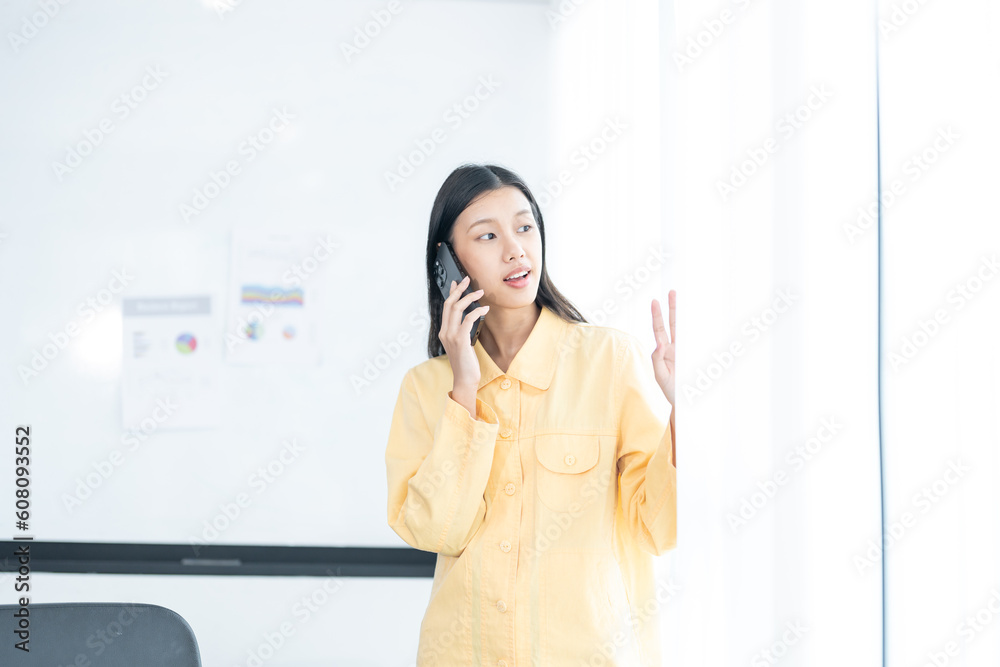 Pretty young Asian business woman standing talking on the phone in the office Pretty young Asian business woman standing talking on the phone in the office