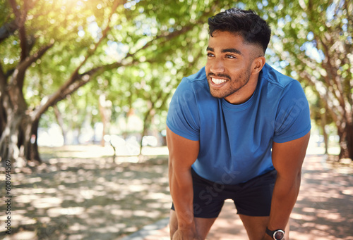 Fitness, break and man or runner outdoor for exercise, training or running at a park. Happy and tired Indian male athlete in nature for a workout, run and rest while thinking of goals or performance