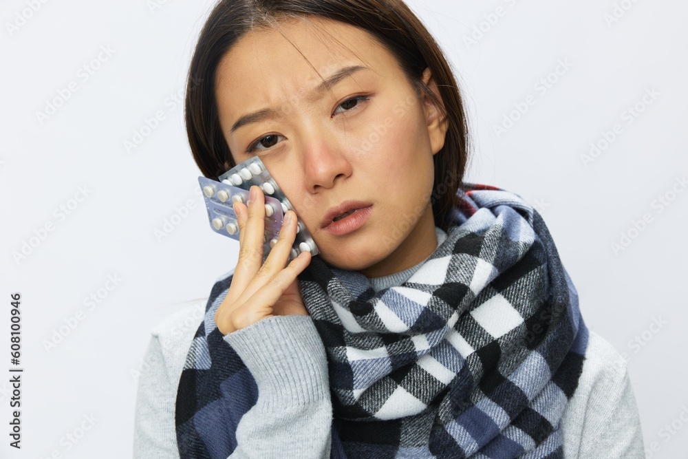 Asian woman headache cold flu holding medicine and pills with fever is sick from the virus on a white background, copy space Asian woman headache cold flu holding medicine and pills with fever is sick from the virus on a white background, copy space