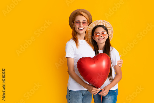 Valentines day. Smiling mother and daughter holding love heart balloon on yellow background. Happy Valentines day to my mom. Love summer.