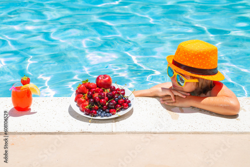 Child eating fruits near swimming pool during summer holidays. Kids eat fruit outdoors. Healthy fruits for children.