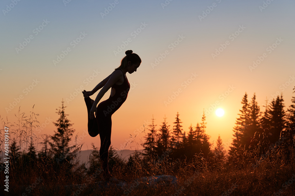 Woman practicing yoga in mountains. Silhouette of young female meditating opposite to sunrise. Early morning workout on fresh air.