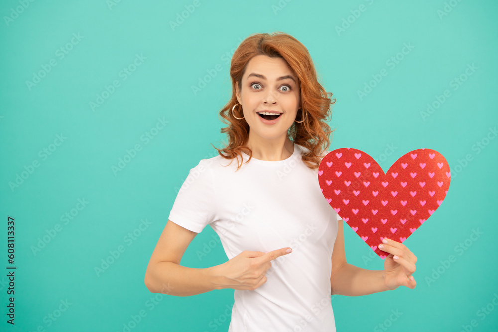amazed young woman with red heart on blue background. point finger amazed young woman with red heart on blue background. point finger