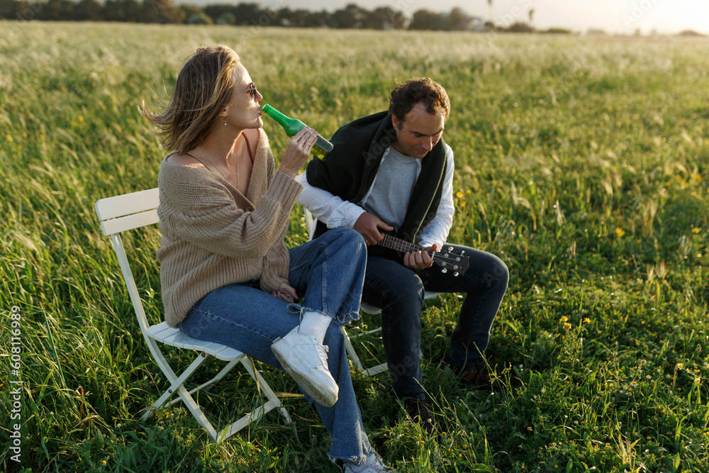 Summer time. Beautiful young couple enjoying time in field around grass. Lifestyle, love, dating, vacation concept. Private. Woman drinking beer, man playing ukulele Summer time. Beautiful young couple enjoying time in field around grass. Lifestyle, love, dating, vacation concept. Private. Woman drinking beer, man playing ukulele