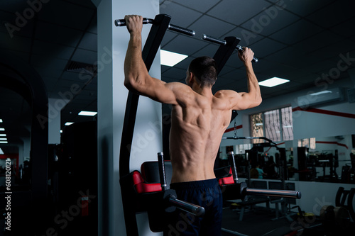 Back view of shirtless man with pull-ups in gym. 