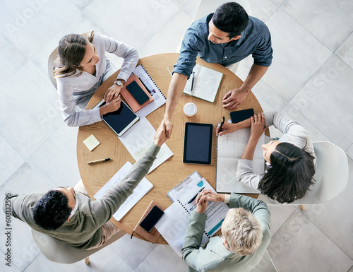 Meeting, handshake and overhead with a business team sitting around a table in the office at work. Partnership, thank you and welcome with male colleagues shaking hands in agreement of a b2b deal