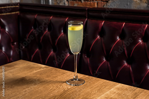 French 75 cocktail made of gin, lemon juice, sugar simple syrup, prosecco sparkling wine served in a flute glass garnished with lemon twist, on a wooden table in restaurant or bar, horizontal photo
