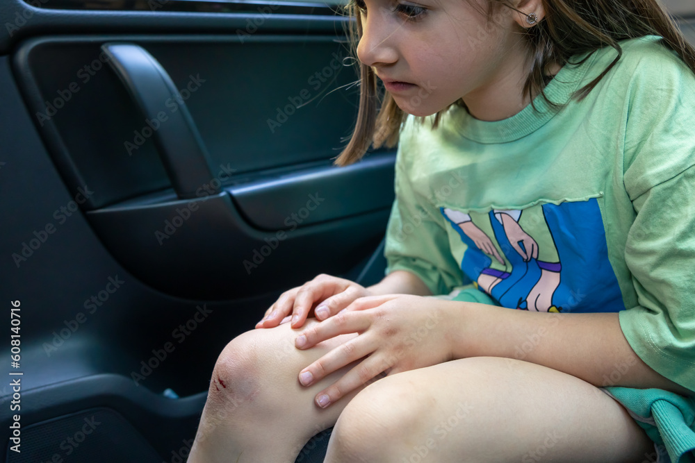 Close-up of little girl holding her bruised injured damaged knee with her hands.