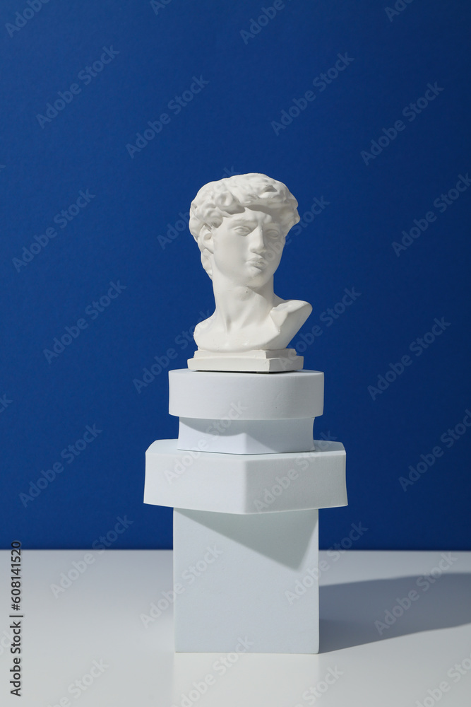 Obraz premium Geometric figures and ancient head on white table against blue background