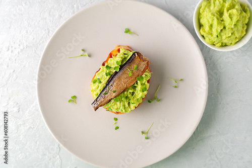 Sandwiches with sprats on toasted slices of bread. Sandwich with smoked sprat - fish, avocado and microgreens. photo