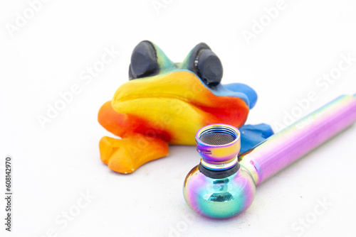 A glass weed smoking pipe and a colorful ceramic frog isolated on a clear background with copy space