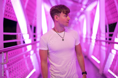 Side view portrait of attractive handsome young man wearing white shirt posing at pedestrian overpass with pink lights.