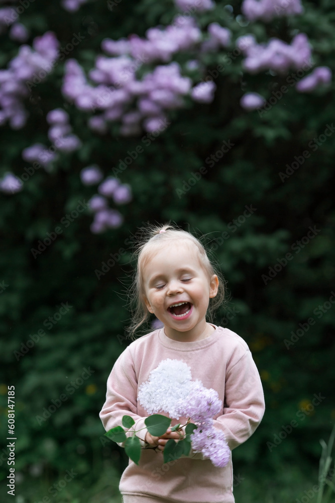 Spring flowering. Portrait of a beautiful little girl 3 years old with lilac flowers in nature. Childhood. The kid poses and looks at the camera. Spring flowering. Portrait of a beautiful little girl 3 years old with lilac flowers in nature. Childhood. The kid poses and looks at the camera.