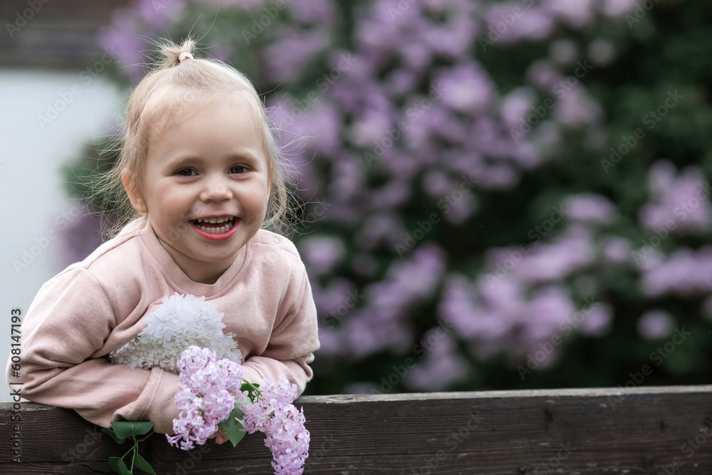 Spring flowering. Portrait of a beautiful little girl 3 years old with lilac flowers in nature. Childhood. The kid poses and looks at the camera. Spring flowering. Portrait of a beautiful little girl 3 years old with lilac flowers in nature. Childhood. The kid poses and looks at the camera.