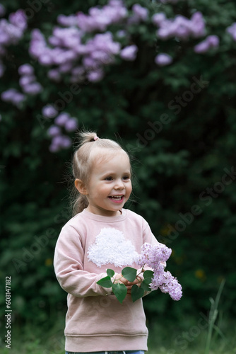 Spring flowering. Portrait of a beautiful little girl 3 years old with lilac flowers in nature. Childhood. The kid poses and looks at the camera.