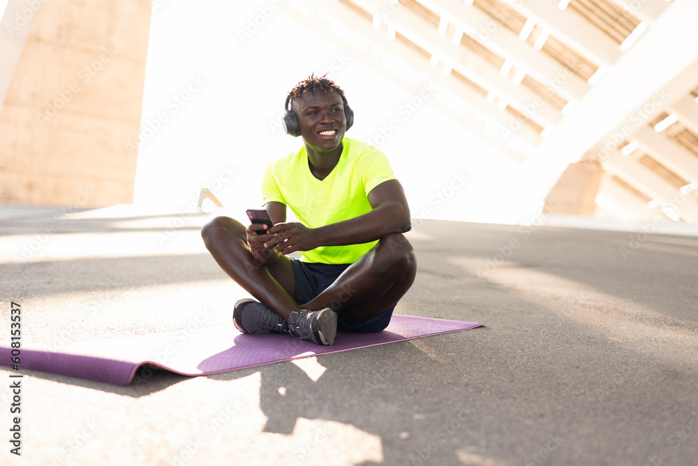 Young athlete man listening music while resting after training. Handsome African man training outside..