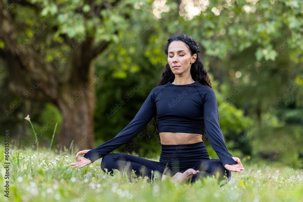 Young beautiful hispanic woman in park sitting on fitness mat and meditating in lotus pose, woman resting after fitness and running with eyes closed, breathing fresh air in tracksuit. Young beautiful hispanic woman in park sitting on fitness mat and meditating in lotus pose, woman resting after fitness and running with eyes closed, breathing fresh air in tracksuit.