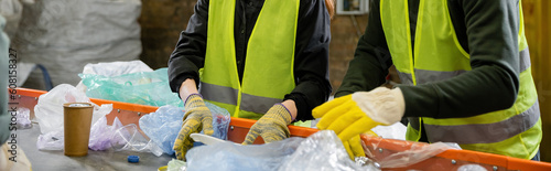 Obraz na plátně Cropped view of sorters in high visibility vests and gloves sorting garbage on c