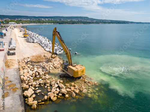 Εκτύπωση καμβά An excavator diligently constructs a dock or breakwater in the sea, its mighty arm reaching out from the shore, creating a resilient structure amidst the waves