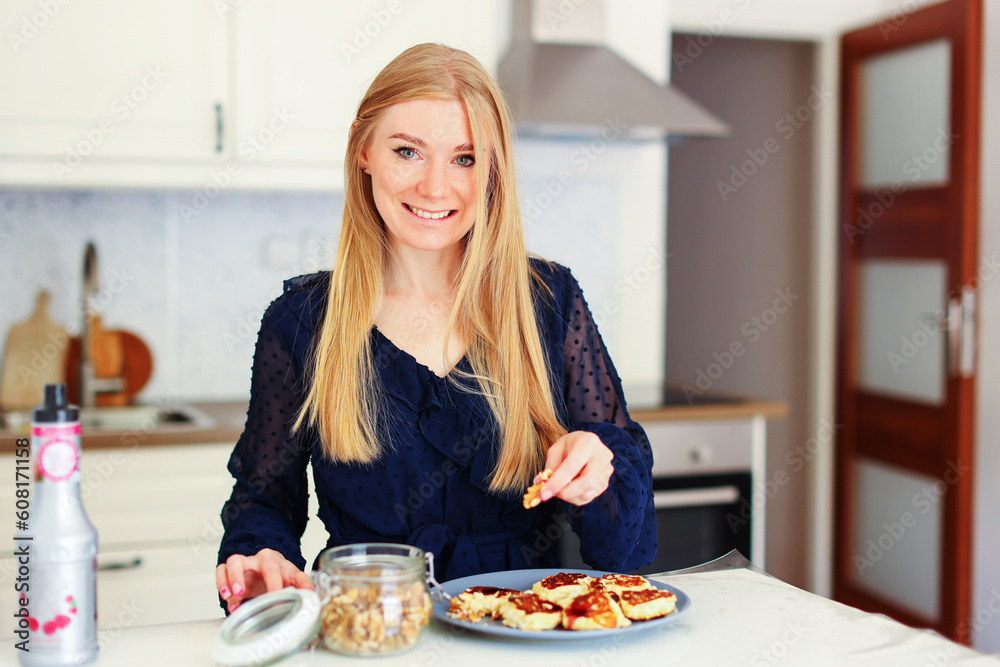happy young woman preparing tasty pancake at the kitchen table in the morning light