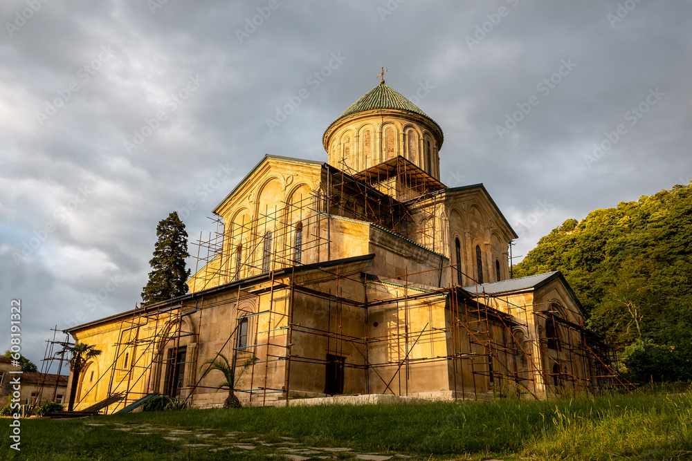 Gelati Monastery, medieval monastic complex near Kutaisi, Georgia founded by King David IV, sunset view with scaffolding during restoration process, dark cloudy sky.