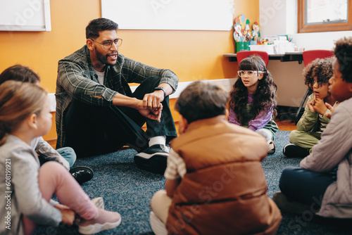 Teacher sitting on the floor with his students in an elementary school classroom photo